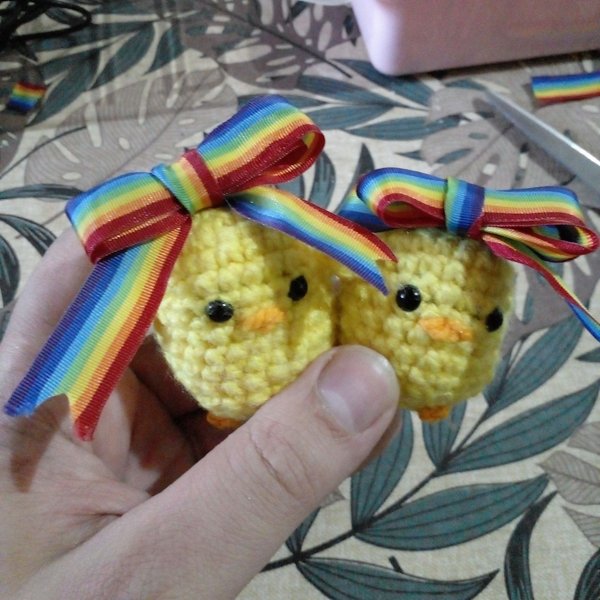 Two amigurumi chickens with pride flag ribbons on their heads.