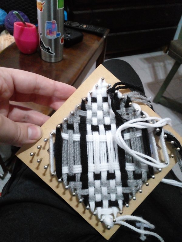 A square pin loom with white-black-grey yarn in a pattern.