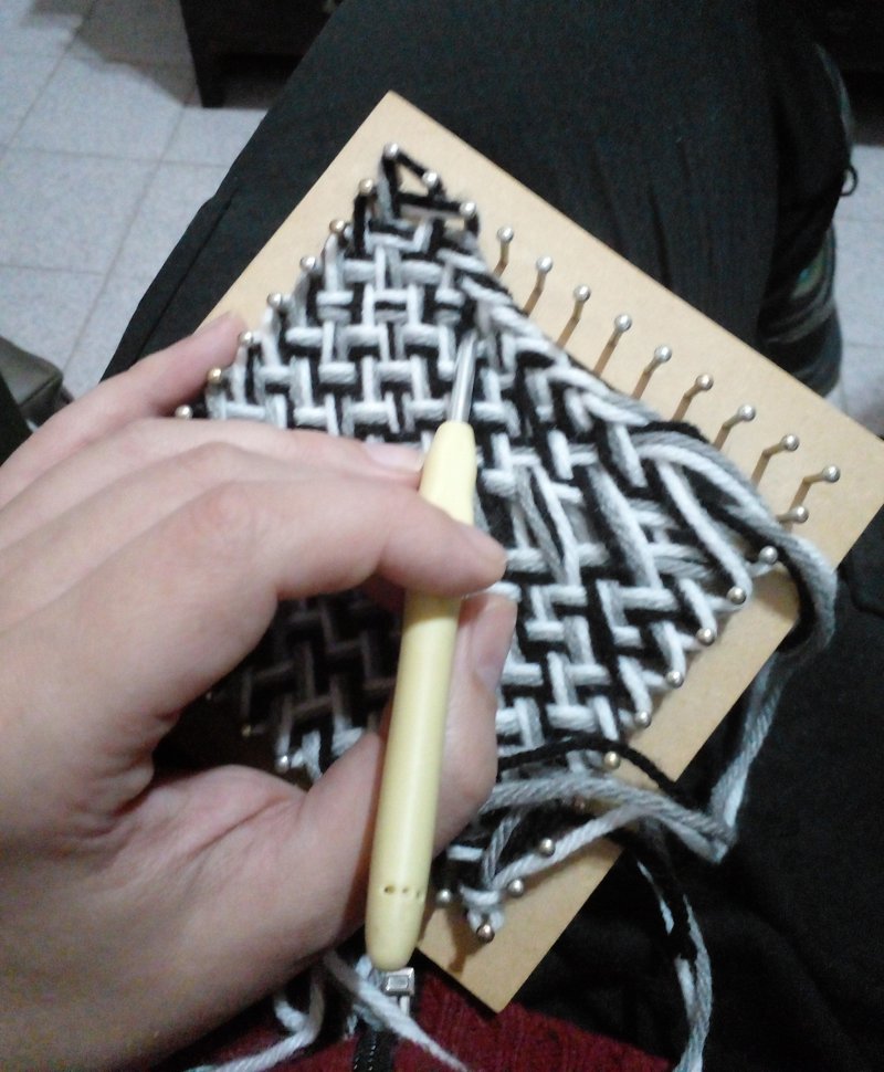 A square pin loom with white-black-grey yarn in a pattern.